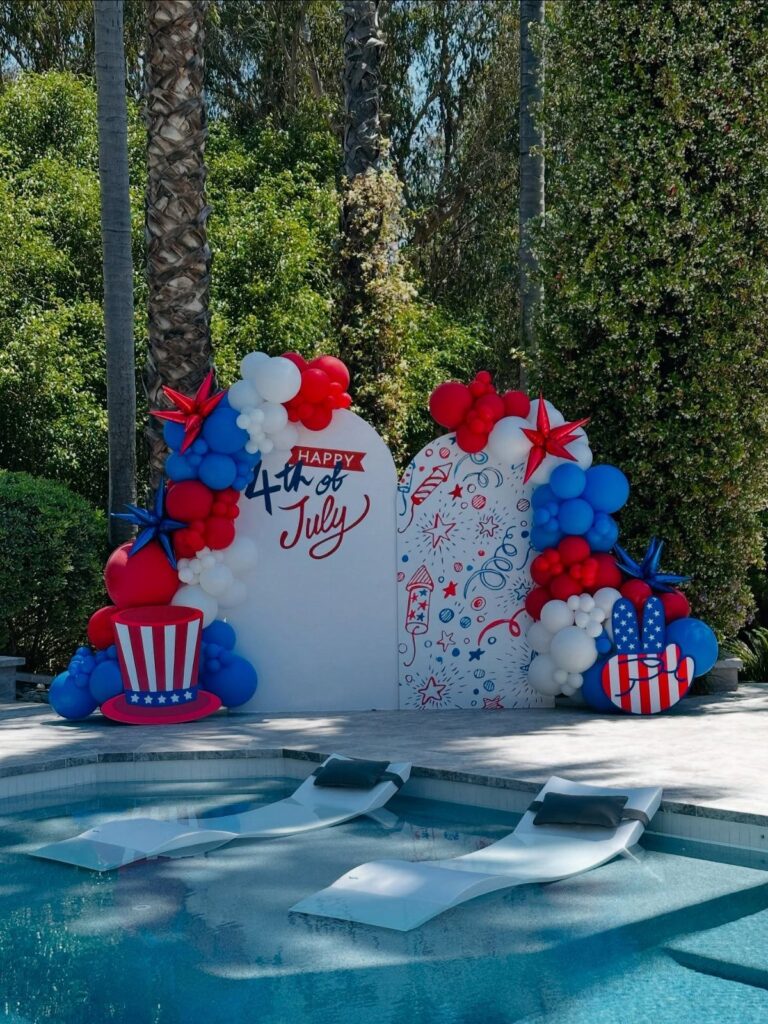 Red, white, and blue balloon decorations and backdrop by a swimming pool.