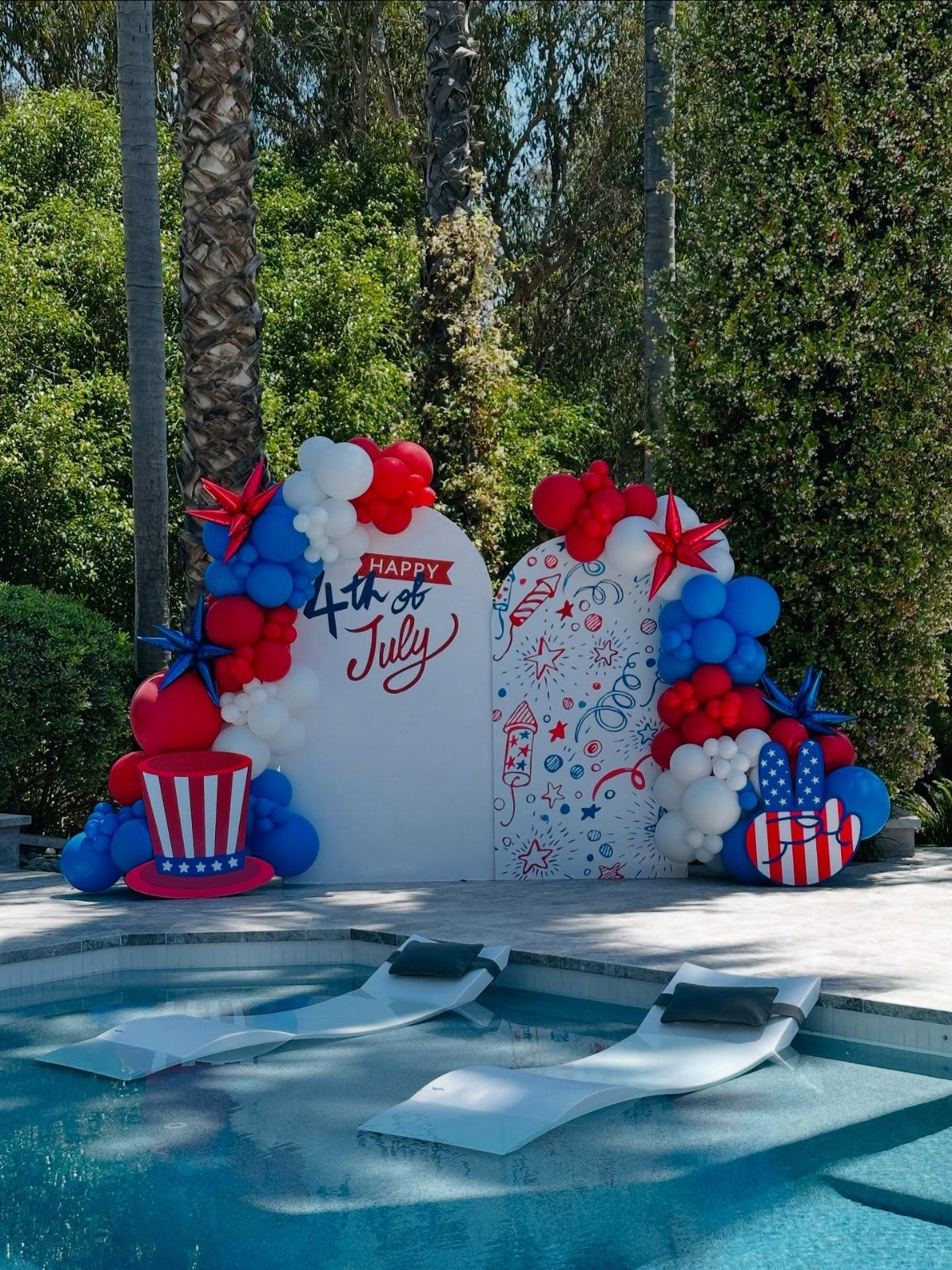 Red, white, and blue balloon decorations and backdrop by a swimming pool.