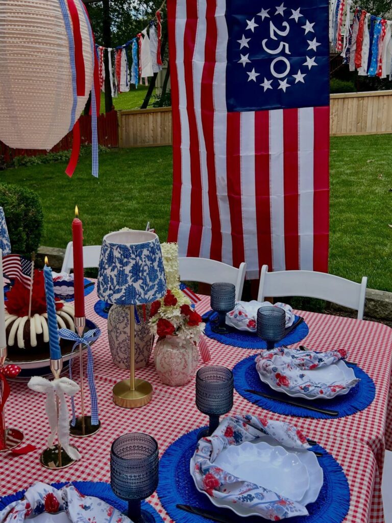 Patriotic table setting with red checkered cloth, blue plates, and American flag background.