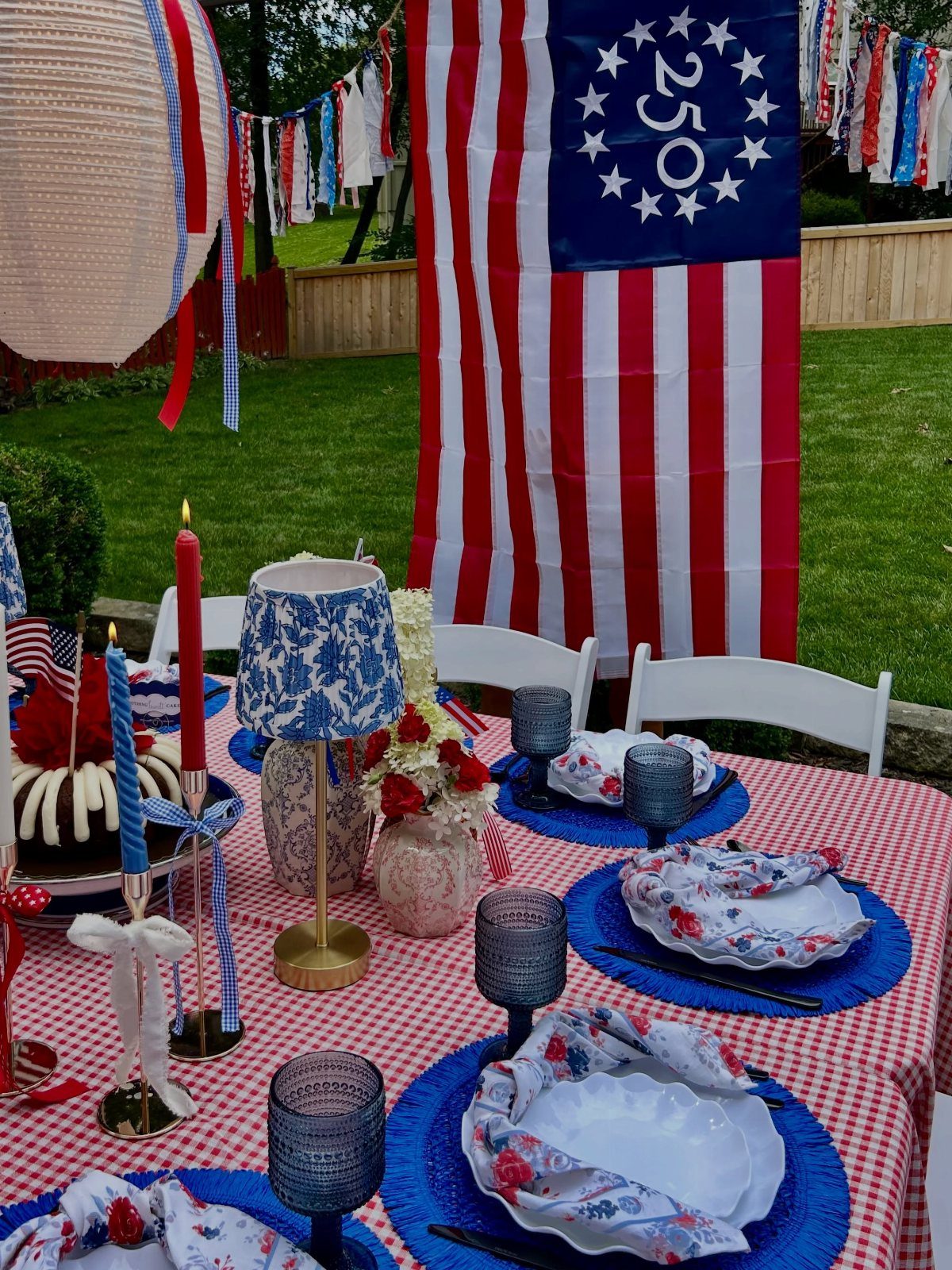Patriotic table setting with red checkered cloth, blue plates, and American flag background.