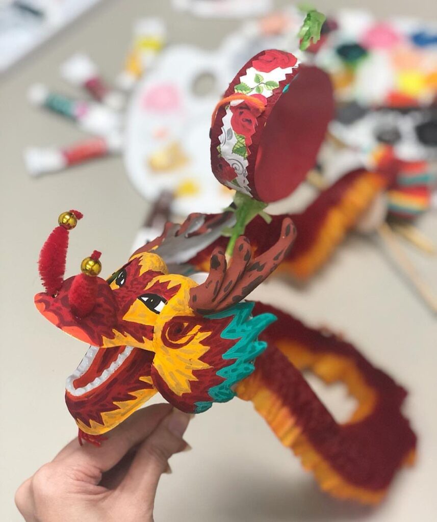 Handmade Chinese dragon puppet with a small red drum held by a hand.