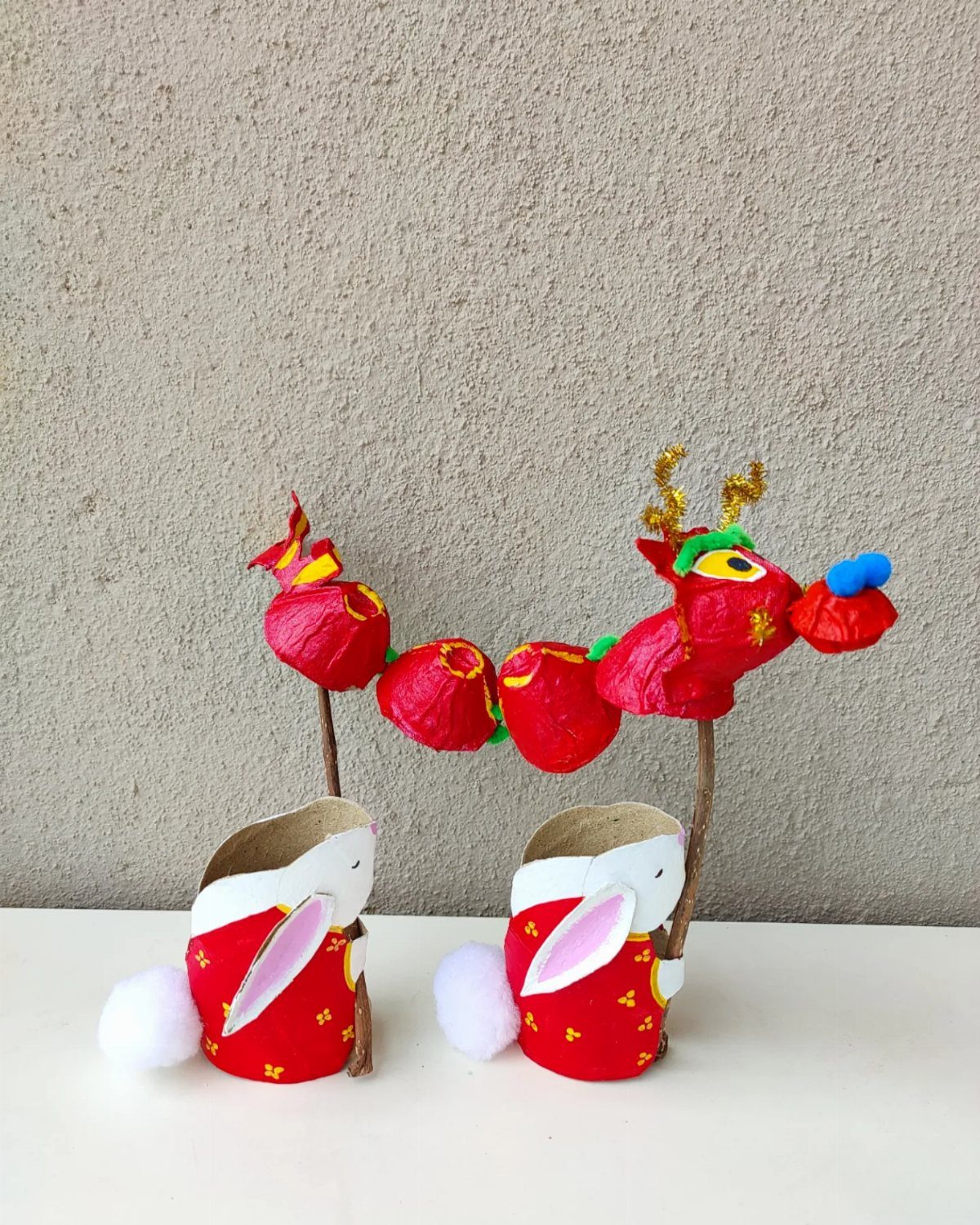 Handmade red dragon puppet held by two small cardboard tube rabbit figures.