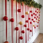 Red and gold ornaments hanging from red ribbons under a lit pine garland.