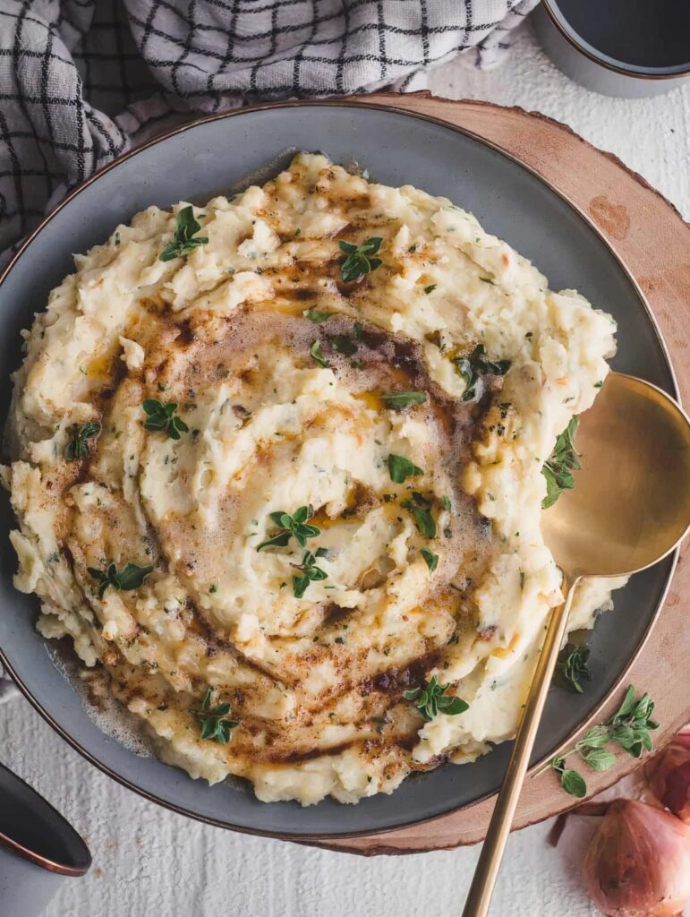 Mashed potatoes with brown butter and herbs in a grey bowl on wood.