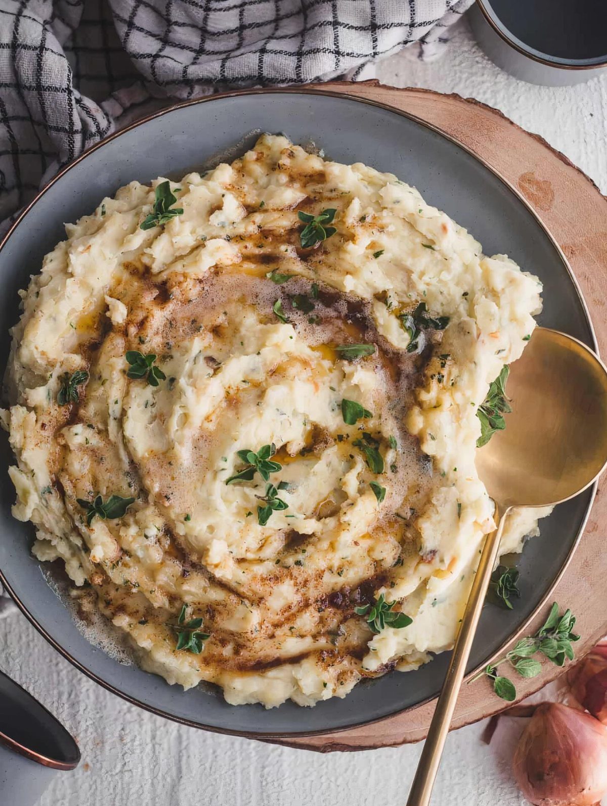 Mashed potatoes with brown butter and herbs in a grey bowl on wood.