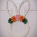 White fluffy bunny wreath with colorful pom-poms hanging on a white door