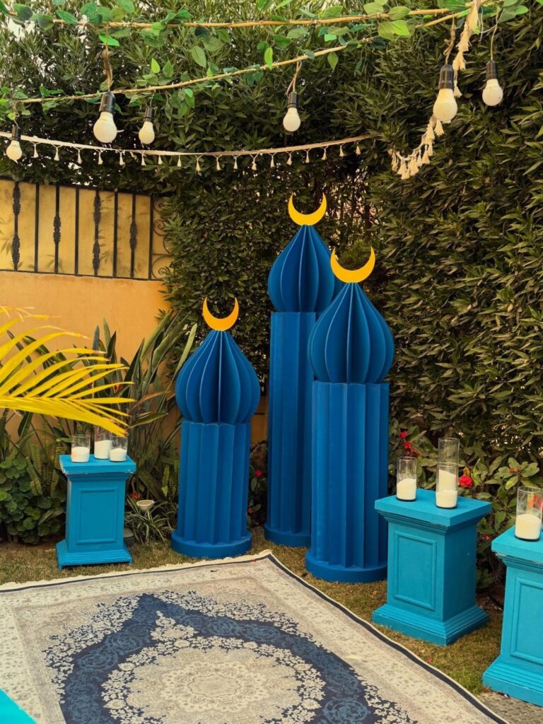 Blue decorative pillars with yellow crescent moons and candles in a garden setting.