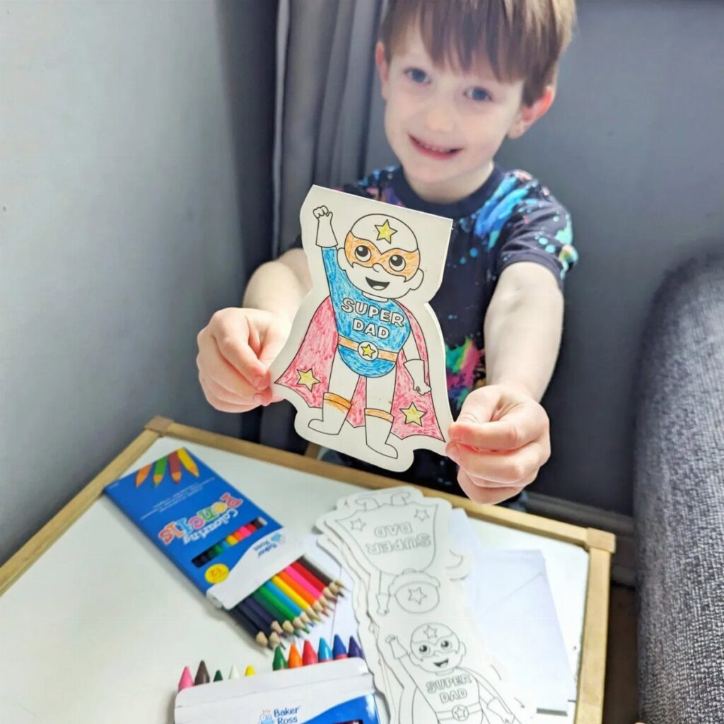 Young boy holding a colorful handmade superhero bookmark that says Super Dad
