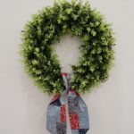 Green boxwood wreath with a red, white, and blue patchwork fabric bow.