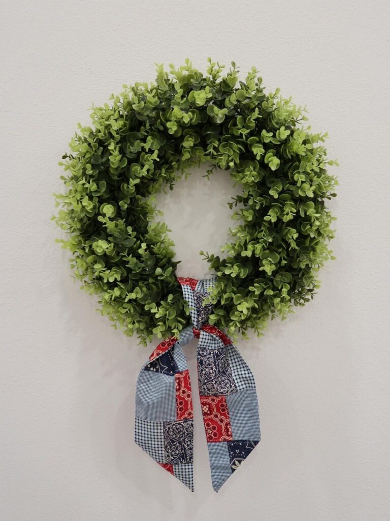 Green boxwood wreath with a red, white, and blue patchwork fabric bow.