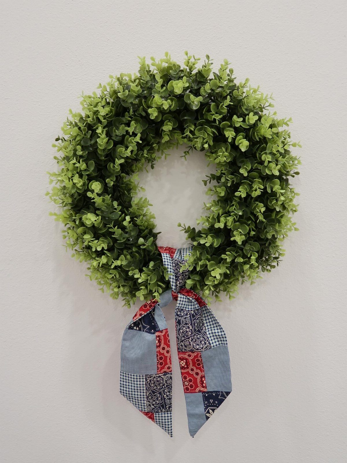 Green boxwood wreath with a red, white, and blue patchwork fabric bow.