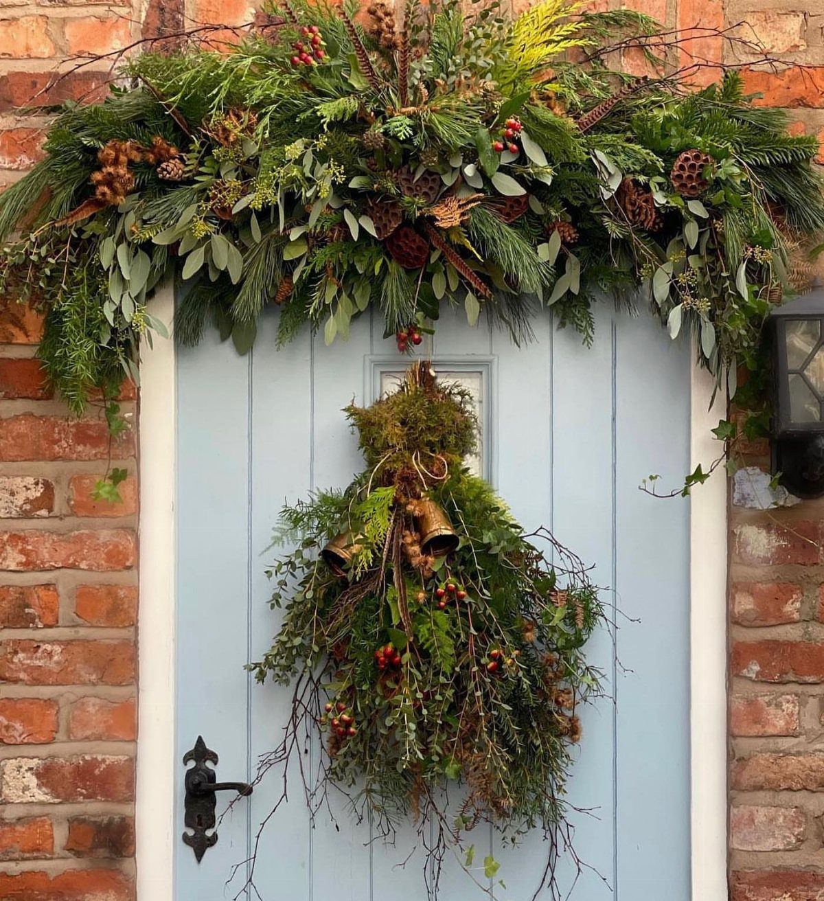 Light blue front door decorated with a lush evergreen garland and hanging swag.