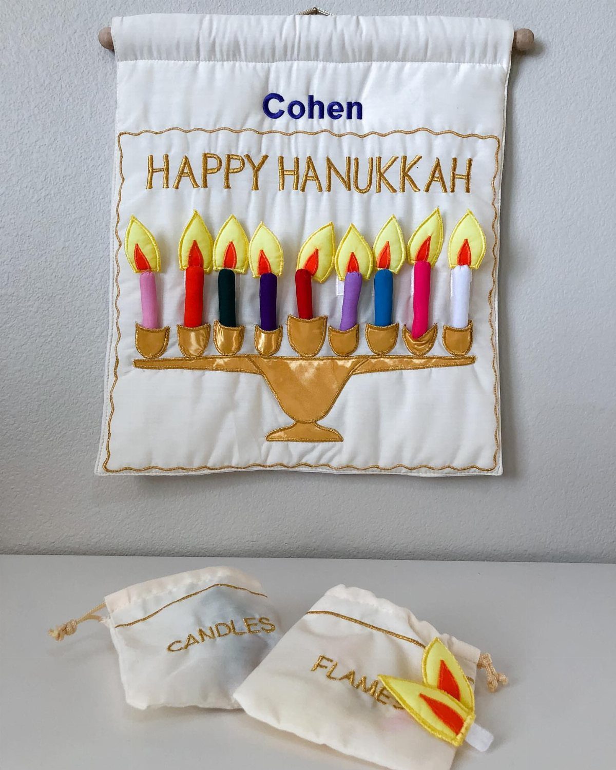 White fabric Hanukkah wall hanging with a gold menorah and colorful felt candles.