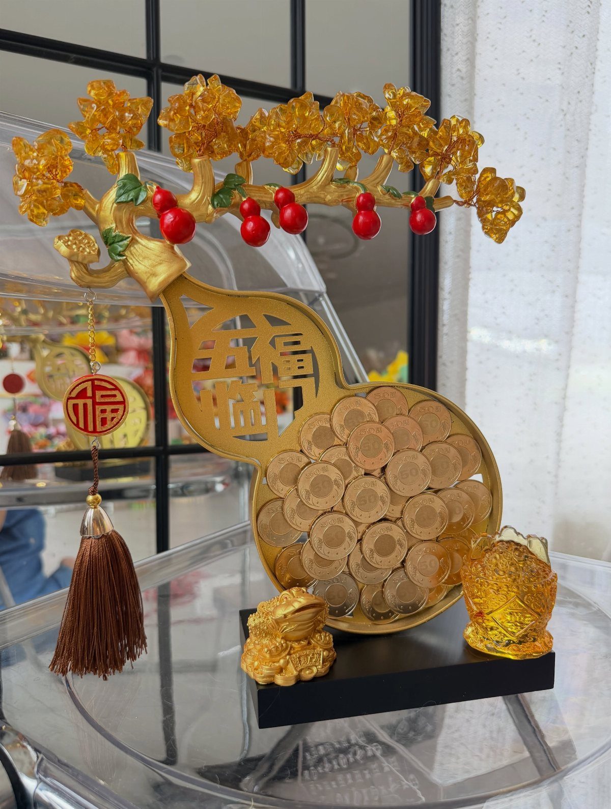 Gold money tree centerpiece with coins, blossoms, and a red tassel on glass.