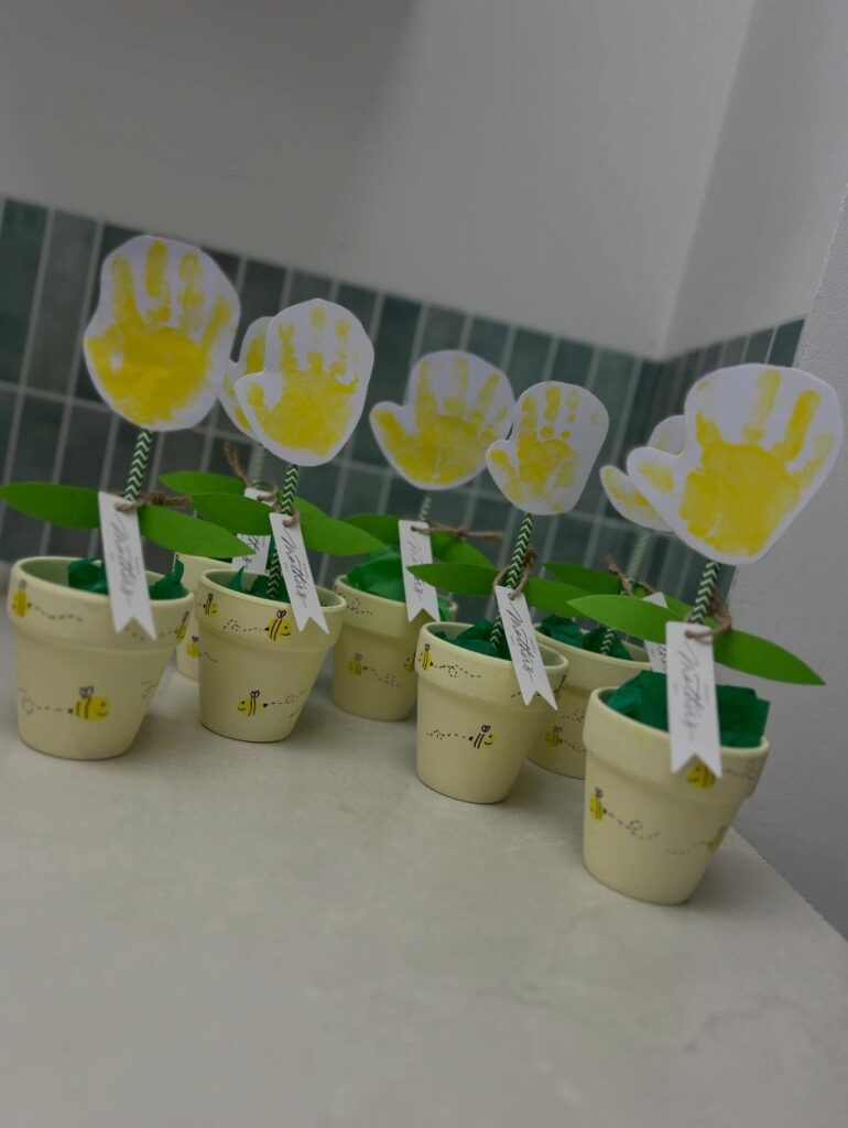 Handprint paper flowers in small cream pots with green stems and white tags.