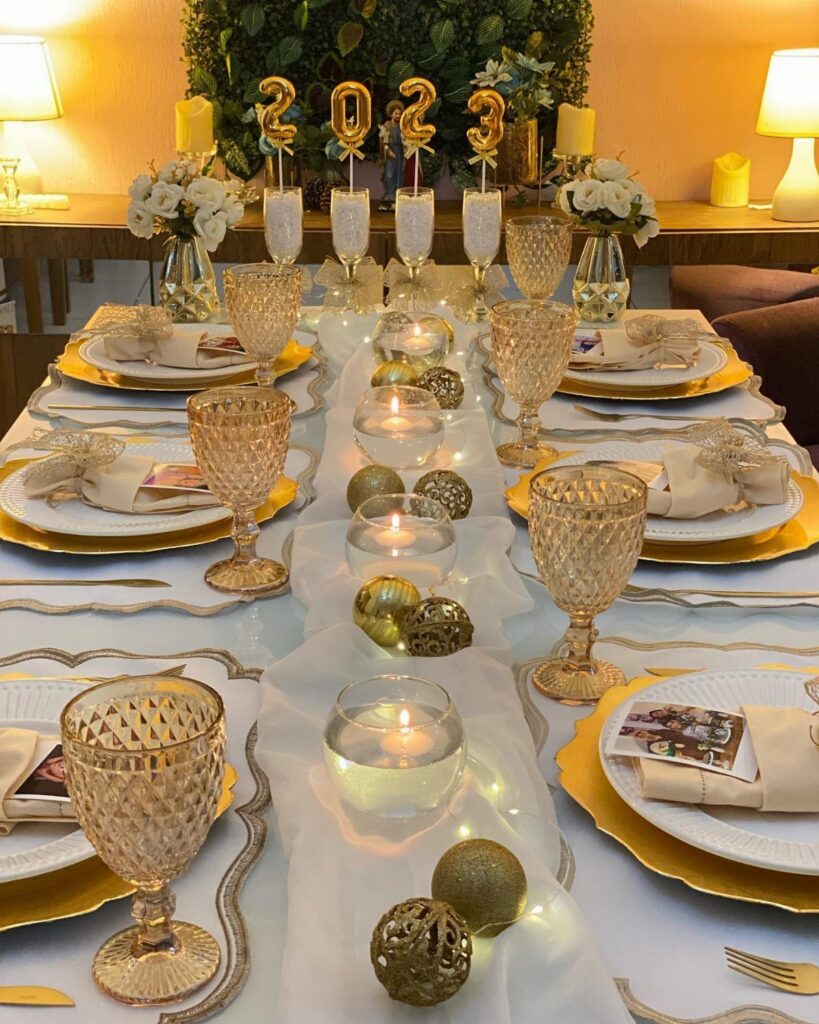 Elegant New Year's Eve table setting with gold accents, candles, and 2023 balloons.