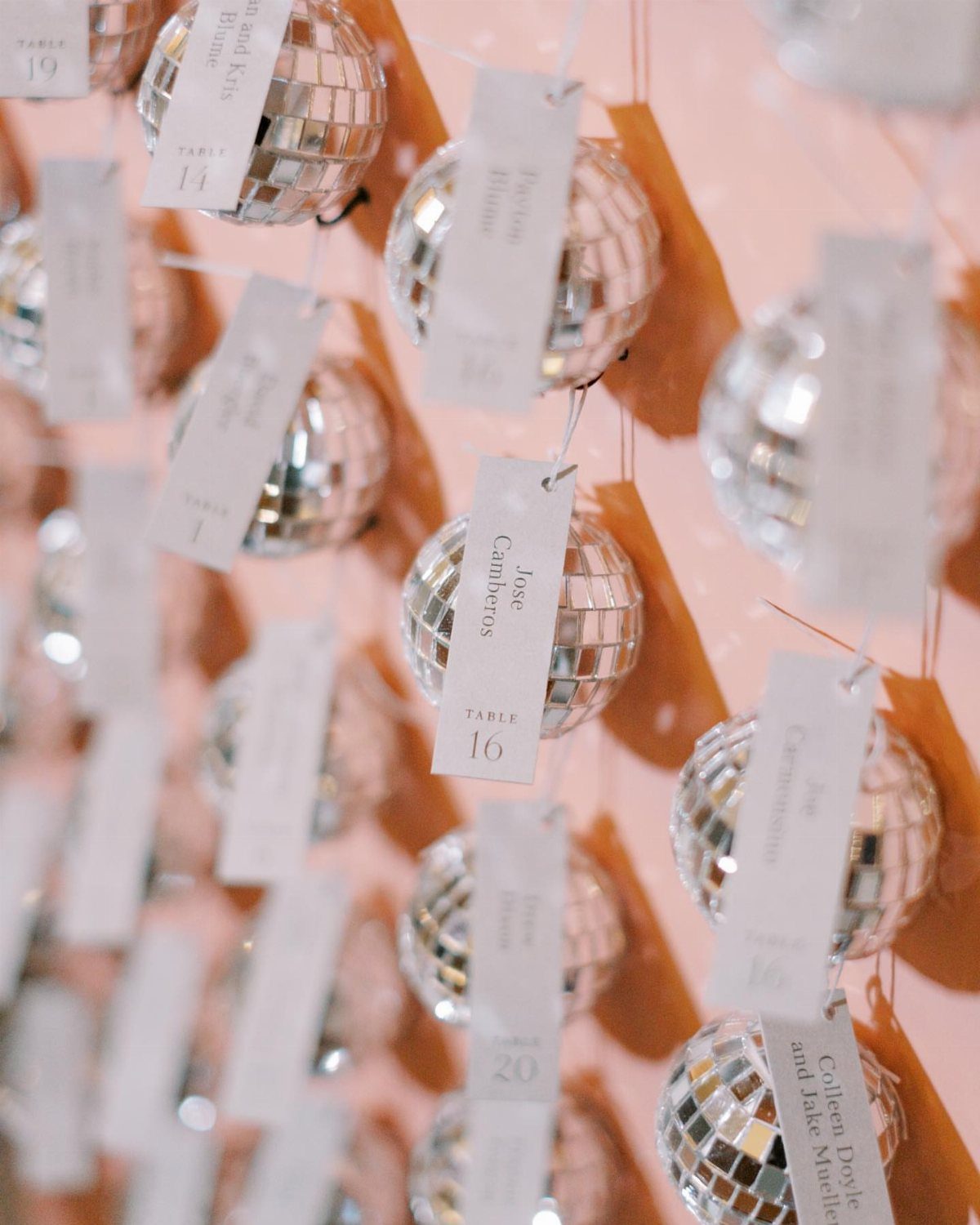 Silver disco ball escort cards with white name tags hanging against peach backdrop