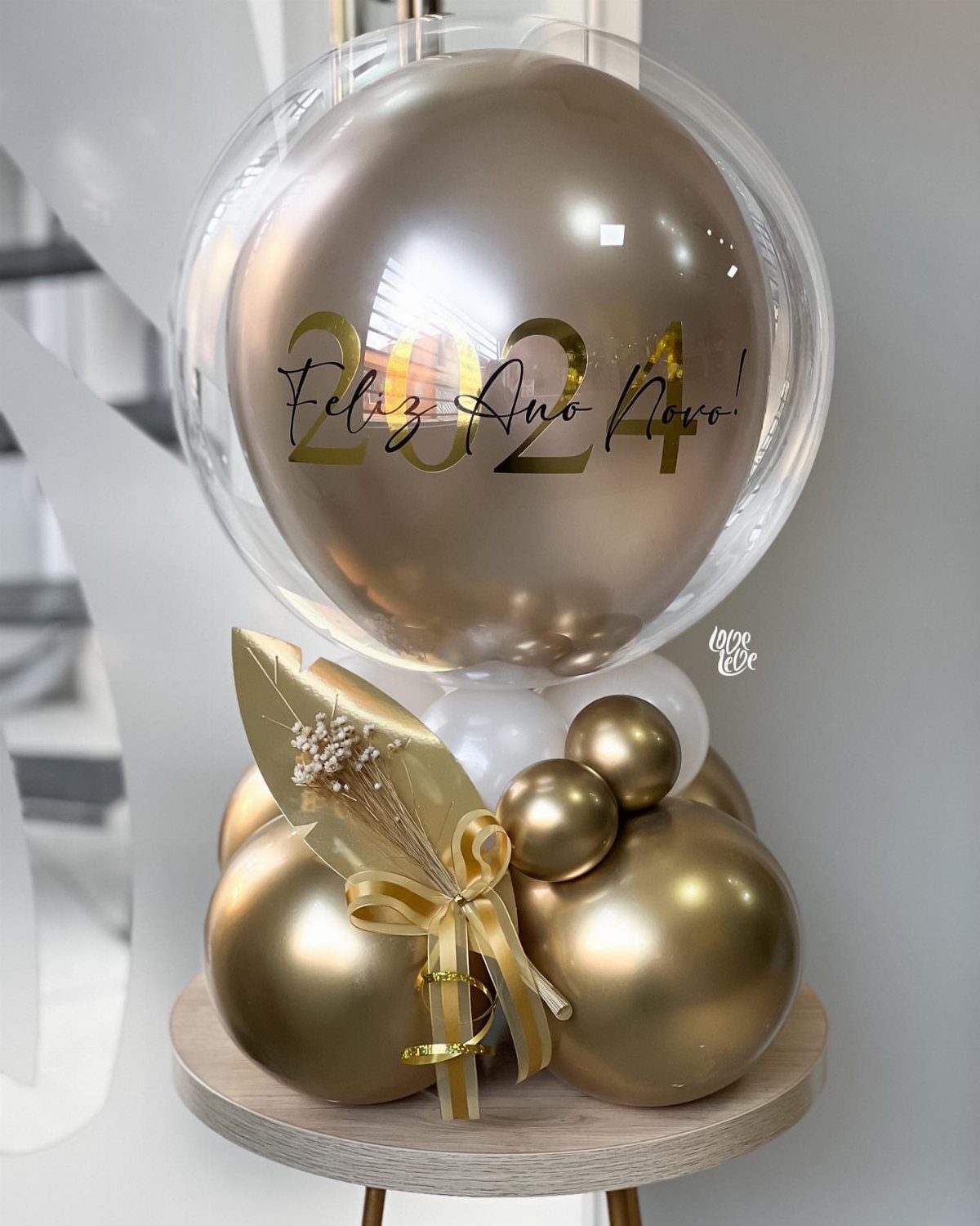 Gold and white balloon centerpiece with 2024 text on a wooden stand.