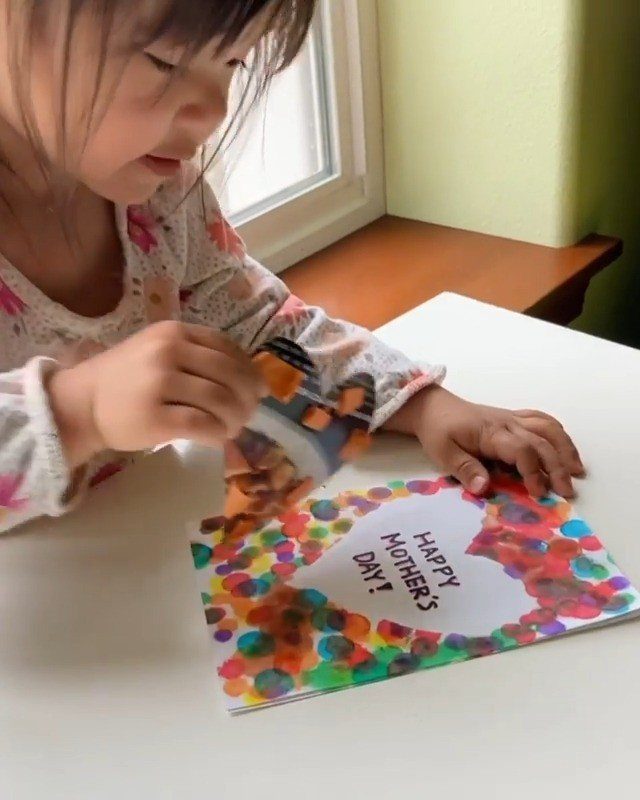 Young child making a colorful dotted Mother's Day card with a heart design.