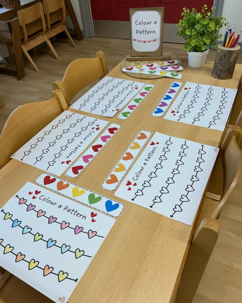 Heart pattern coloring pages and colored strips on a wooden classroom table.