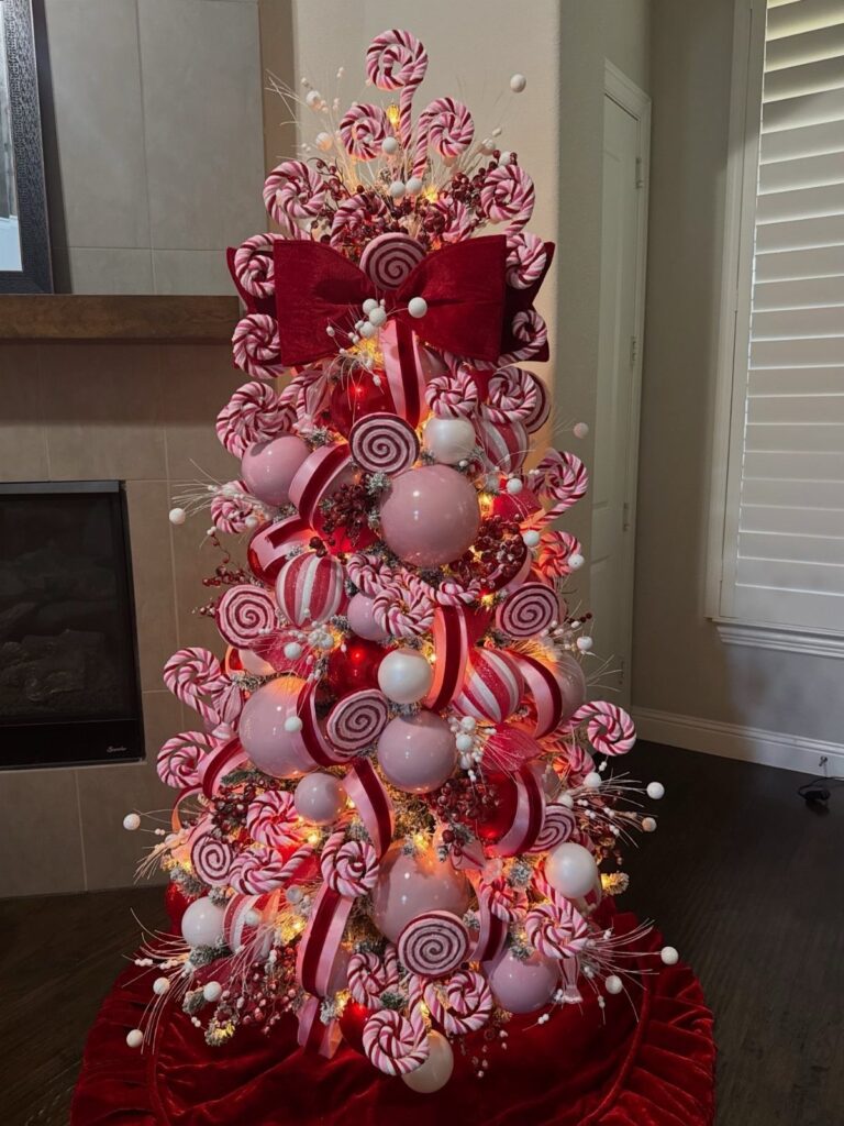 Christmas tree decorated with pink and red lollipop ornaments and a large red bow.