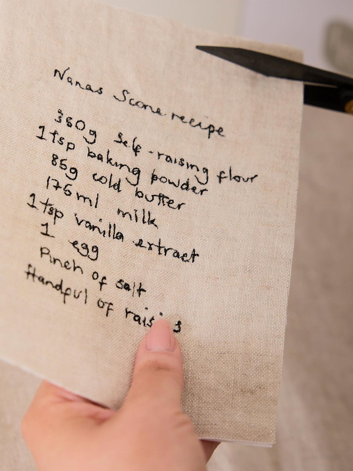 Beige linen kitchen towel with a handwritten scone recipe written in black ink.