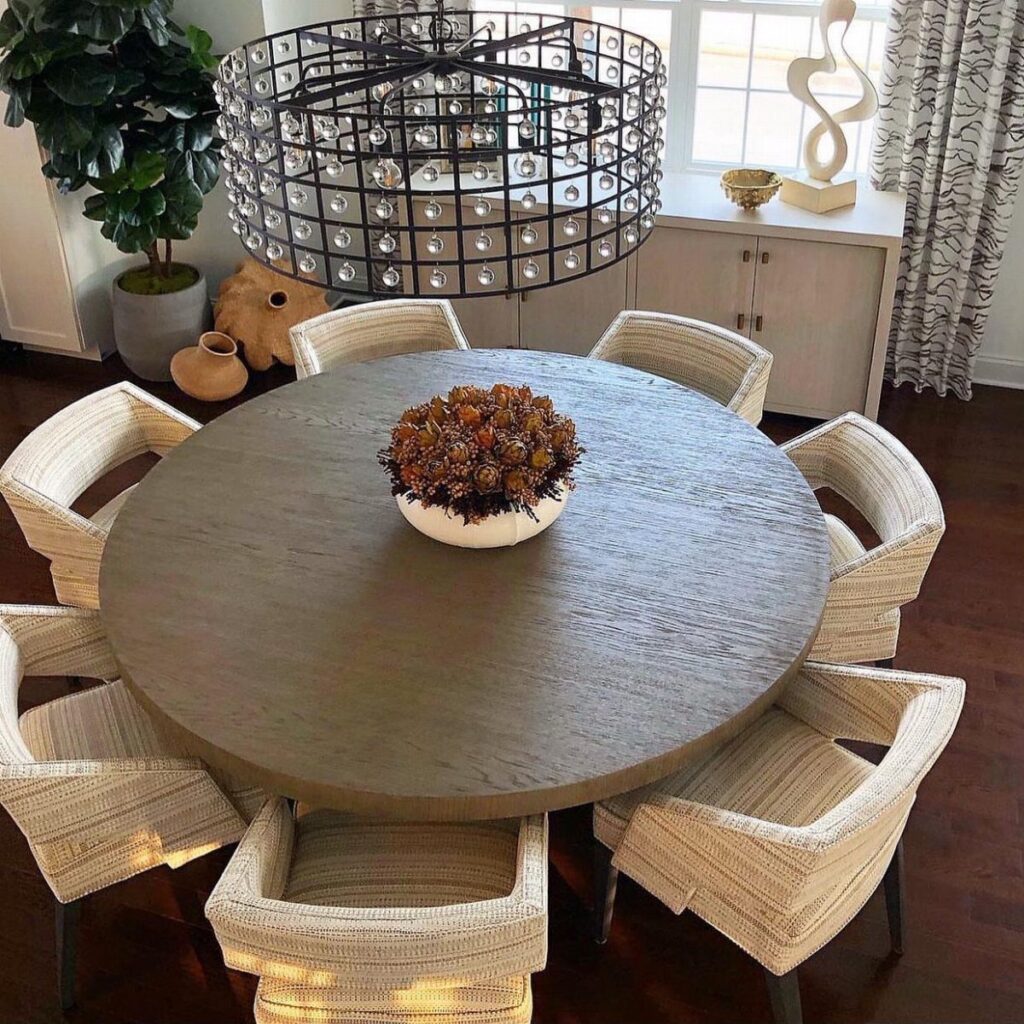 Round grey wooden dining table with autumn foliage centerpiece and woven white chairs.