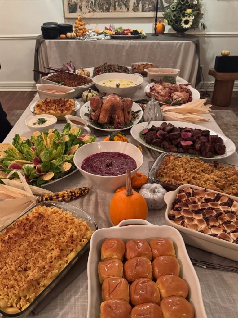 Thanksgiving feast spread on a grey tablecloth with roasted turkey and autumn decorations.