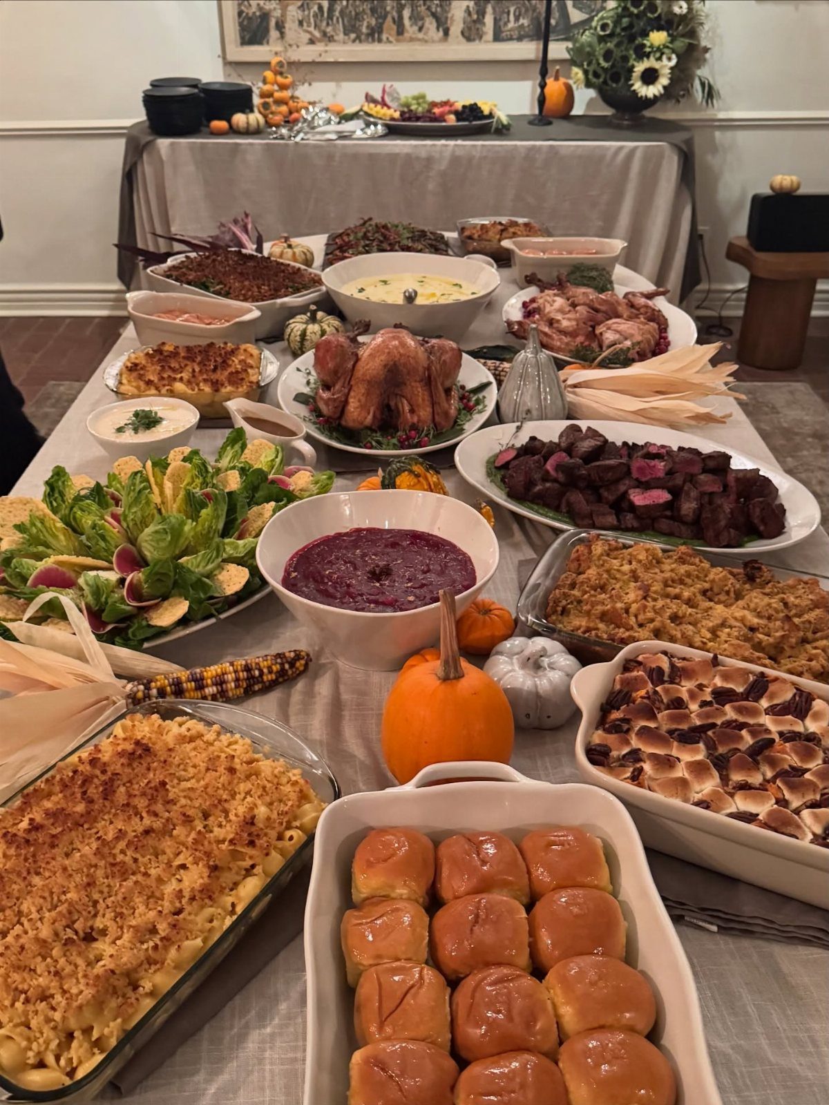 Thanksgiving feast spread on a grey tablecloth with roasted turkey and autumn decorations.
