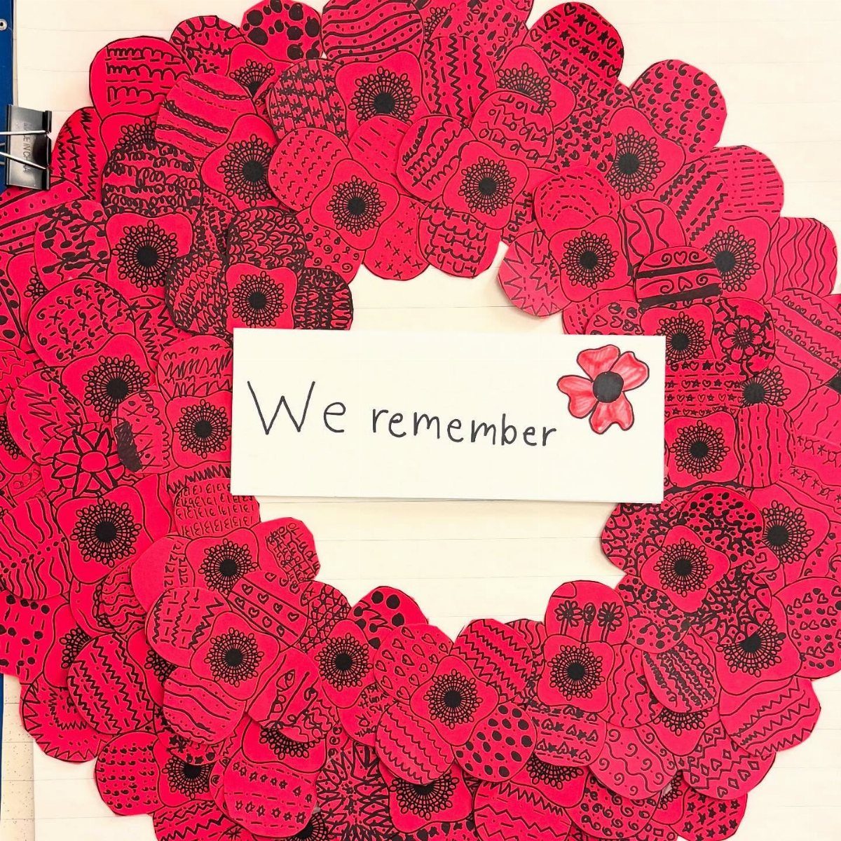 Red poppy wreath surrounding a white card that says We remember.