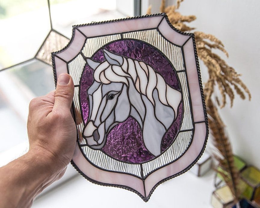 Stained glass horse suncatcher with purple background held up by a hand.